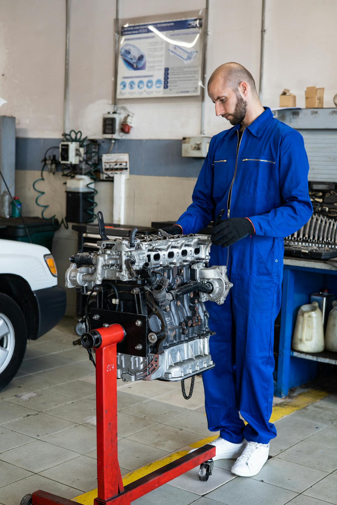 Male mechanic in blue coverall inspecting engine in an automotive repair workshop.