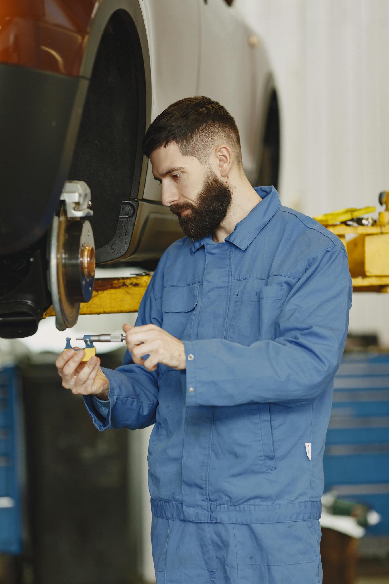 Mechanic in blue uniform inspecting car brakes in garage setting.