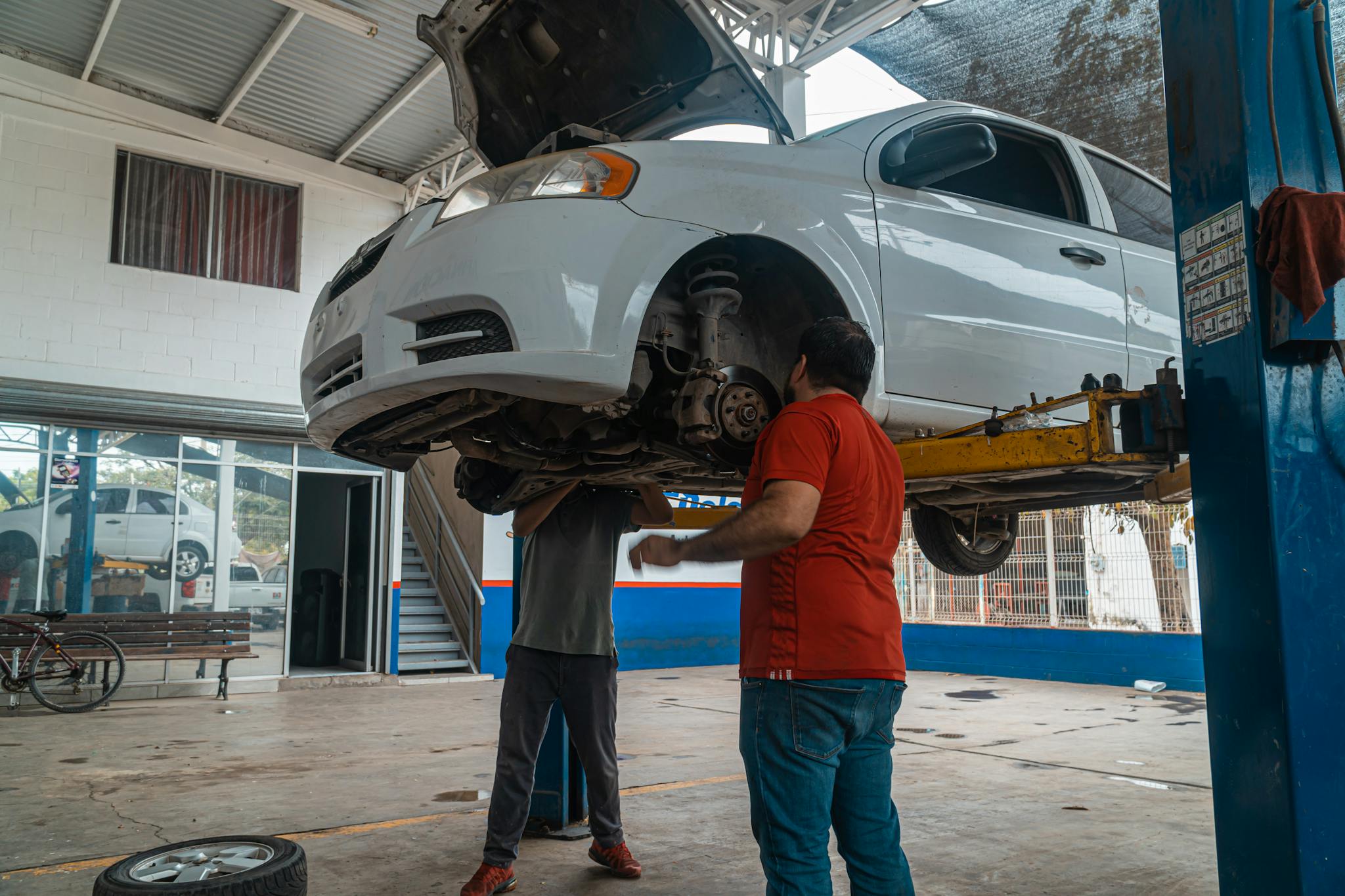 Two mechanics inspecting a white car on a lift inside a garage workshop.